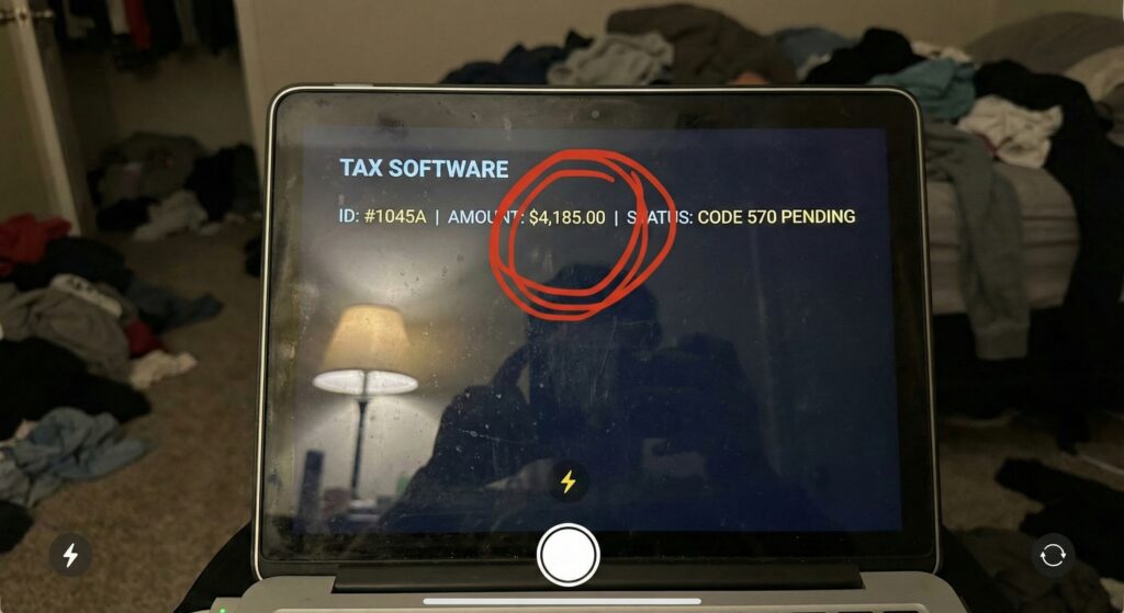 A smudged laptop screen displaying an IRS tax transcript with Code 570 highlighted, showing a frozen refund status in a dimly lit room.