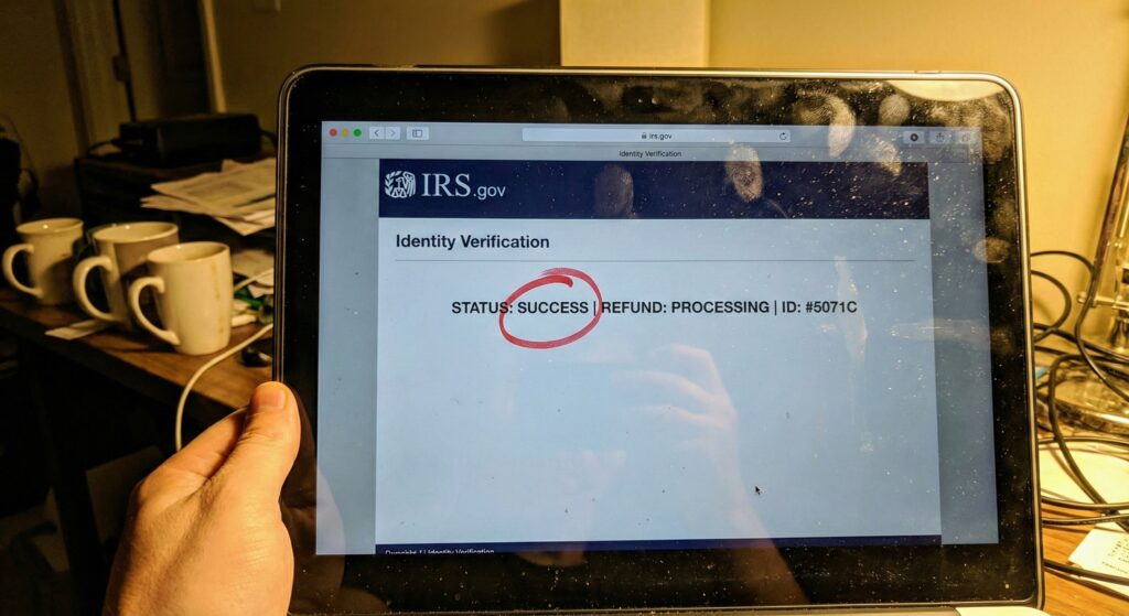 A smudged laptop screen displaying the IRS id.verify success message in a dimly lit home office.