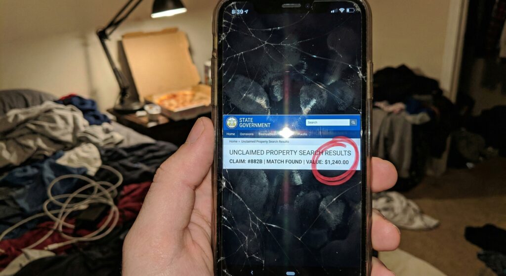 Cracked smartphone screen displaying a state unclaimed property map with dollar signs.